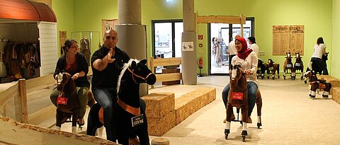 Hier wären Studierende zu sehen, die auf Spielzeugpferden reiten. Diese Station war Teil der Sonderausstellung "Cowboy und Indianer" des Badischen Landesmuseum Karlsruhe.