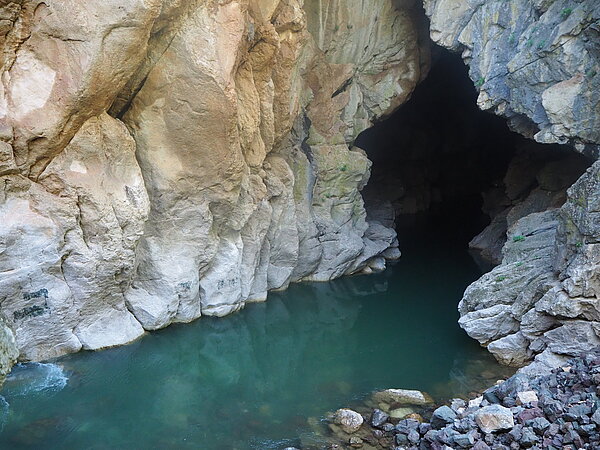 Ein schmaler Flussarm verschwindet in einer tiefen Steinhöhle. Die Felsen über dem Fluss unmittelbar vor der Höhle wurden zum Teil geglättet und an mehreren Stellen mit assyrischen Reliefs versehen (gut sichtbar ist das Relief des Königs Tiglatpileser zentral am linken Bildrand).