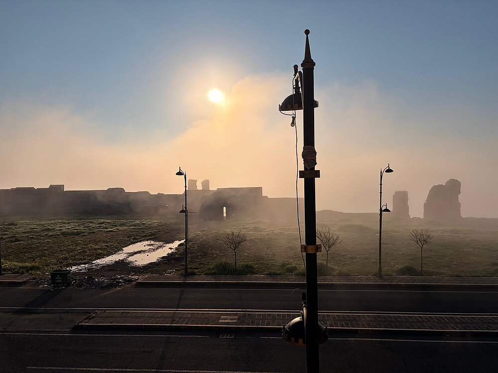 Auf der anderen Seite einer Straße erhebt sich im Morgennebel eine halbverfallene Festung.