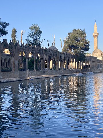 Ein großer Teich mit einem Säulengang ummauert; am hinteren Teichrand erhebt sich ein Minarett.