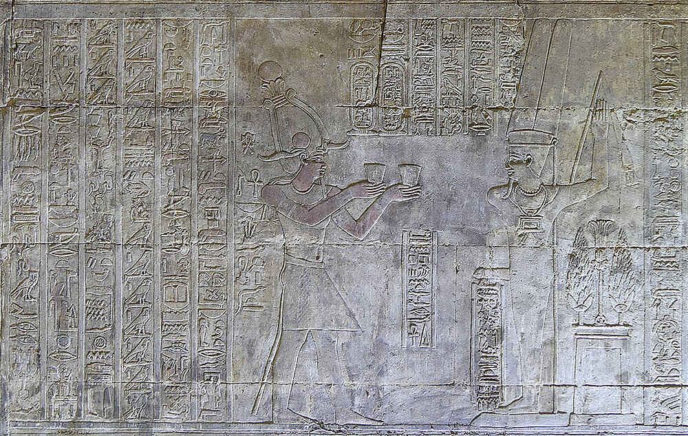 Der König, Ptolemaios IV. Philopator (221–205 v. Chr.), opfert dem Min mnhp-Substanz (eine Art Aphrodisiakum) mit einem langen, das Ritual begleitenden Hymnus auf Min hinter dem König. Ritualszene in der Min-Kapelle des Edfu-Tempels.