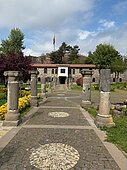 Ein von Säulen gesäumter Weg führt zentral durch eine Parkanlage auf das ehemalige Kasernengebäude aus Stein zu.