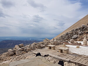 Auf einer kargen Bergkuppe stehen Köpfe überlebensgroßer Statuen eines Adlers und einer Gottheit. Im Hintergrund ist der Blick von der Bergspitze über eine Tal- und Gebirgslandschaft zu sehen.